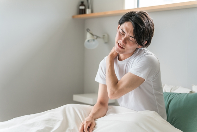 ベッドに腰かけて肩を押さえる男性