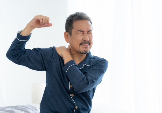 腕を上げて肩を押さえる中年の男性